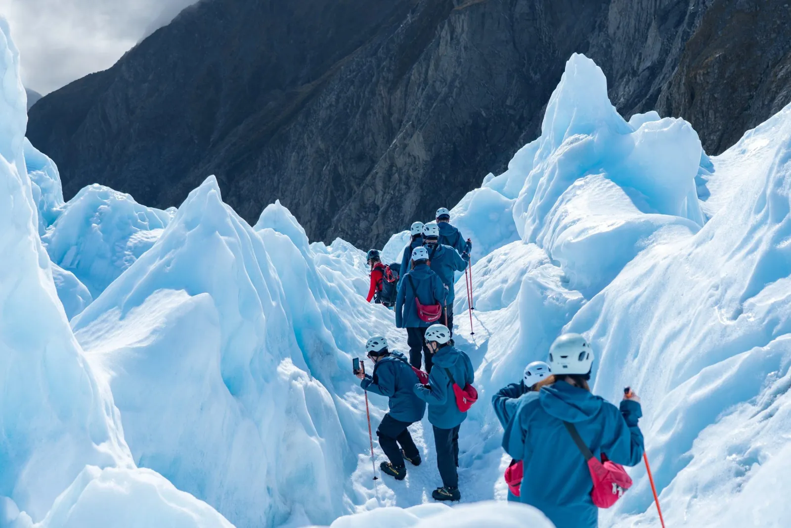 Group of hikers in helmets climbing a path between tall blue ice pinnacles