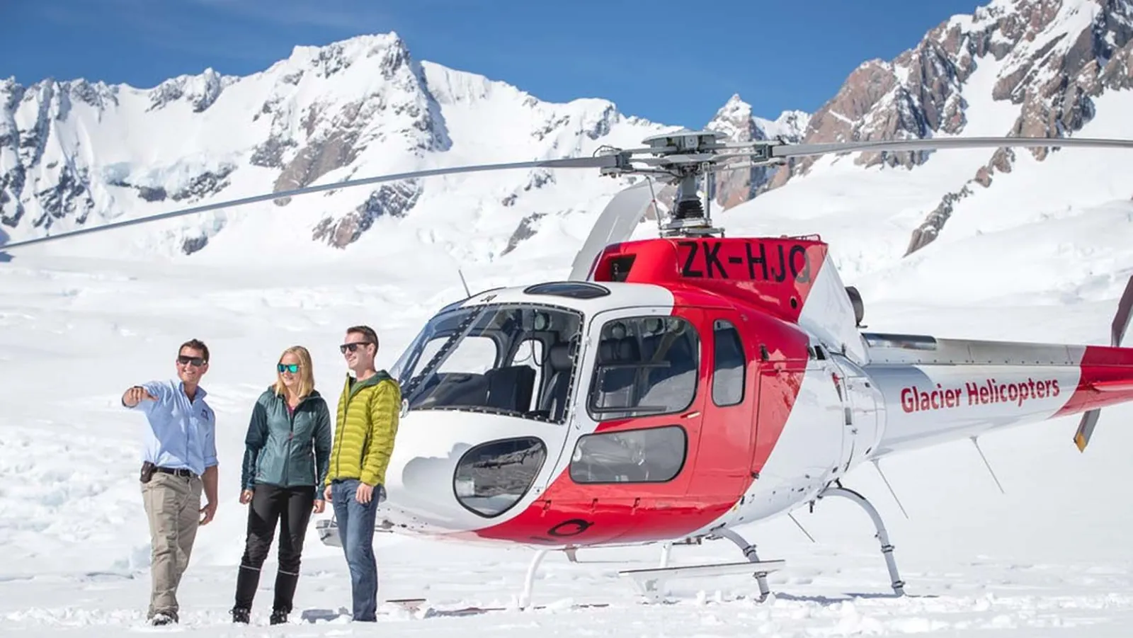 Three visitors and a pilot standing in front of a red and white helicopter on snow