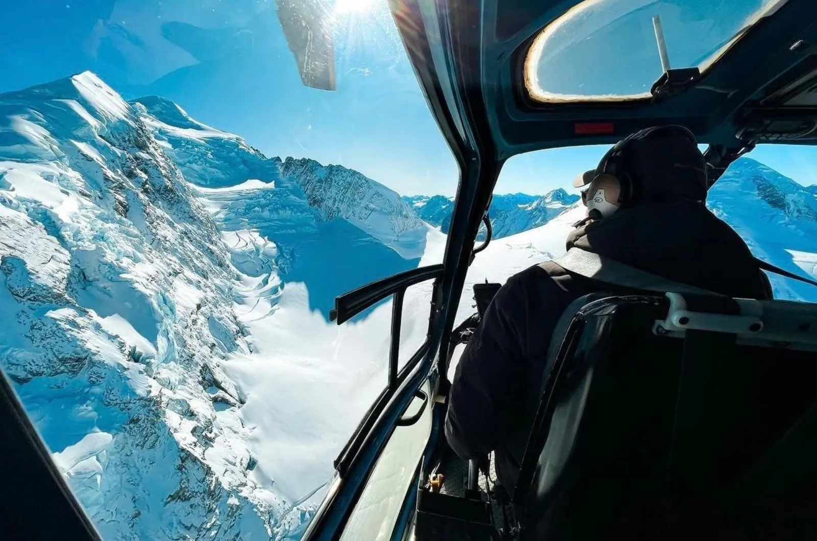 View from inside a helicopter cabin of steep snowy ridges and glaciers under blue sky