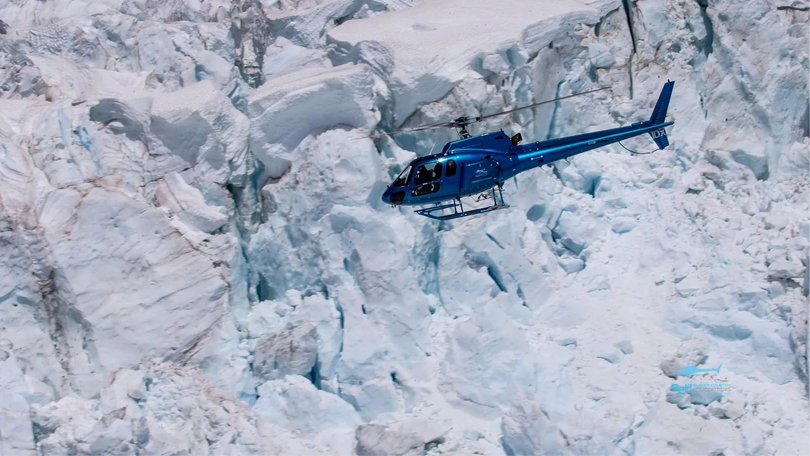 Blue helicopter flying low over a jumble of broken blue-white glacier ice