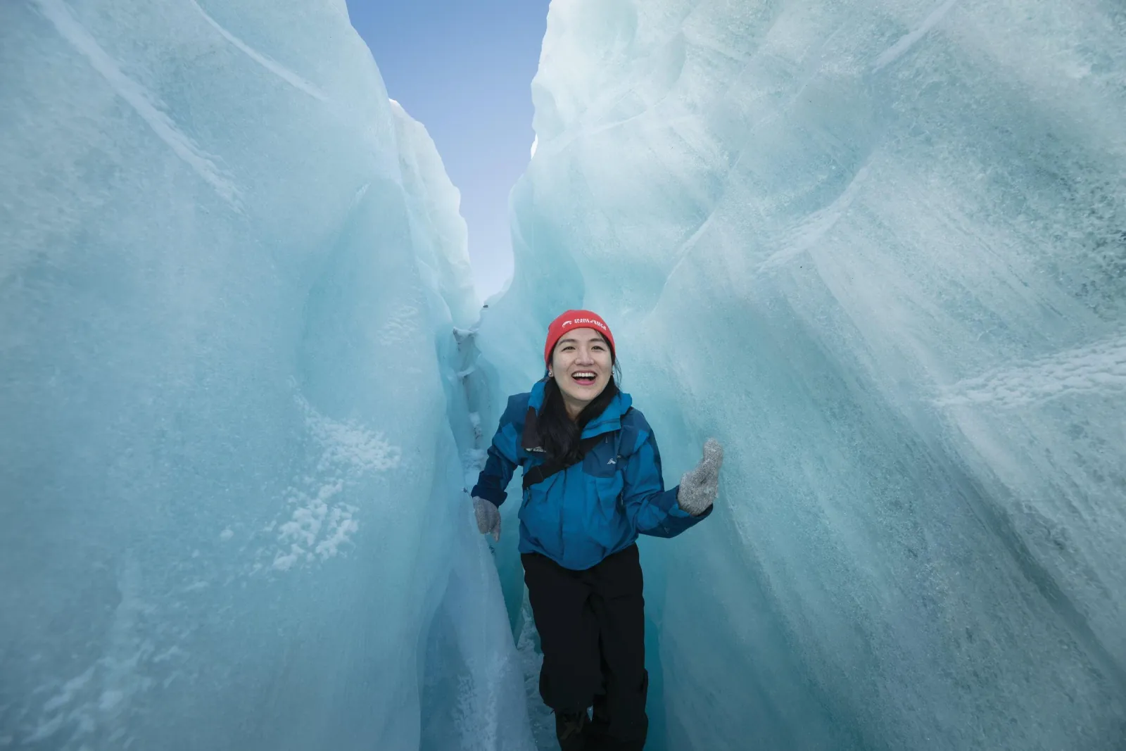 Smiling woman in red beanie and blue jacket standing in a narrow blue ice slot