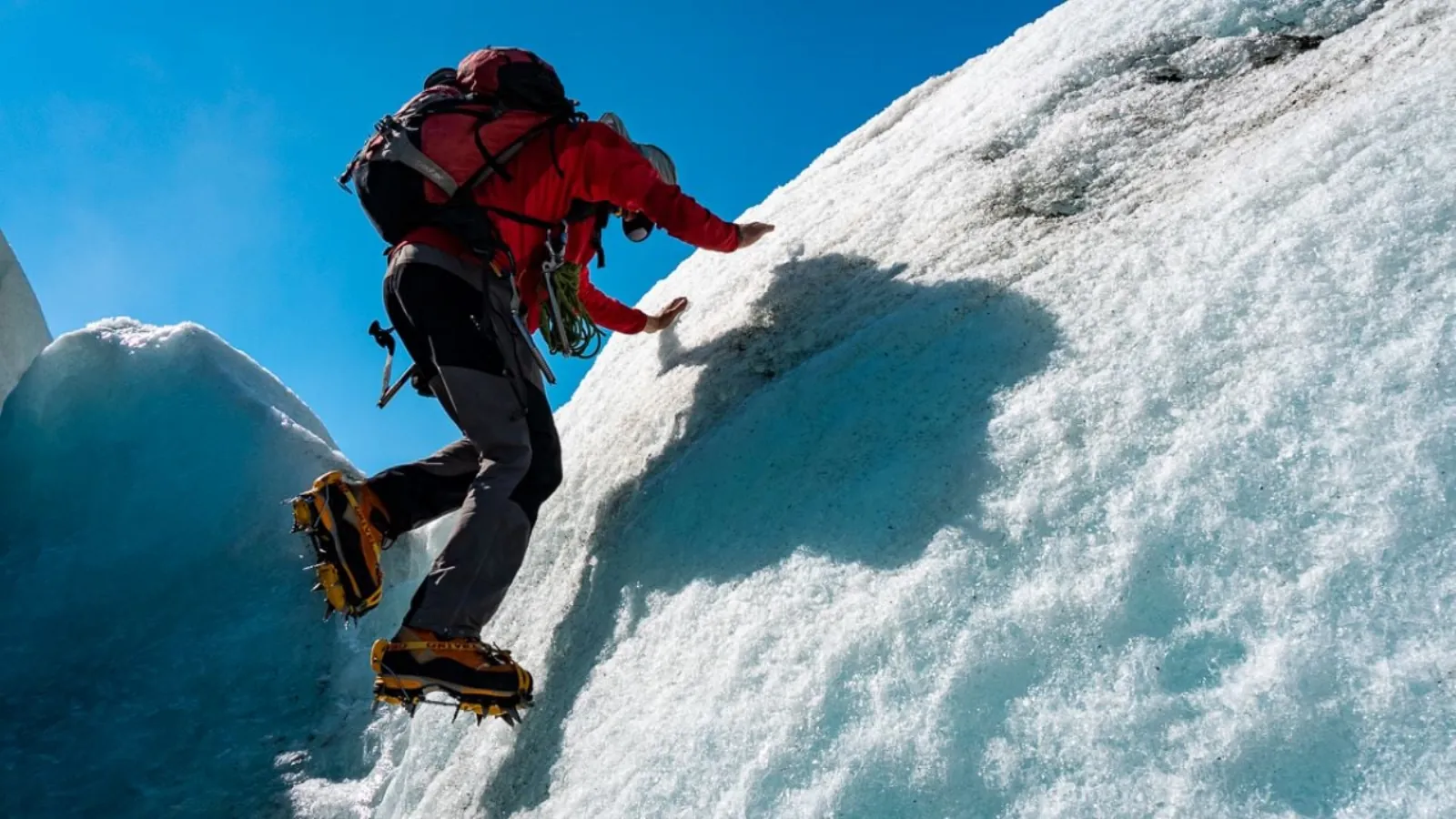Climber in red jacket and crampons scaling a steep snow and ice slope
