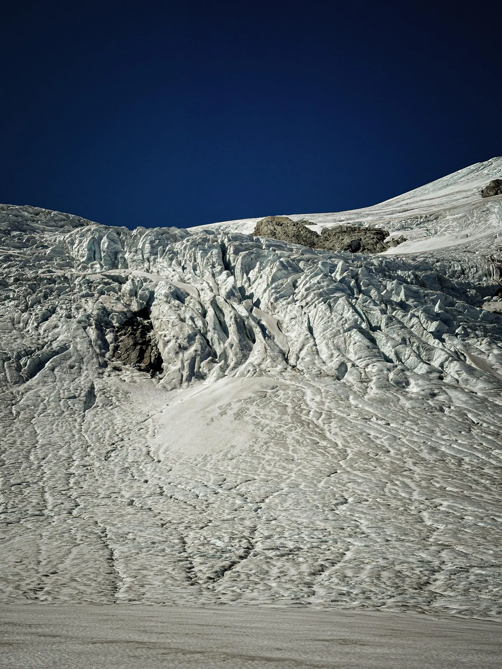 Close view of crevassed grey-white glacier ice under a deep blue sky