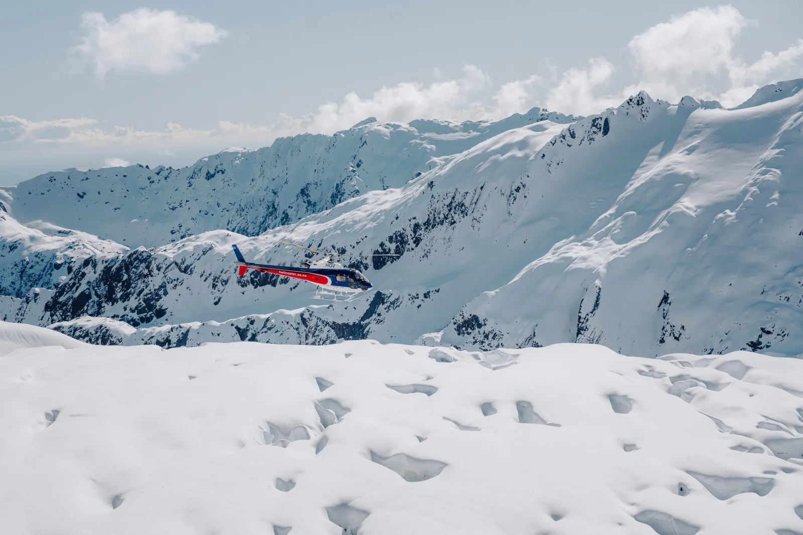 Helicopter flying low over a snowy alpine ridge with footprints in the foreground