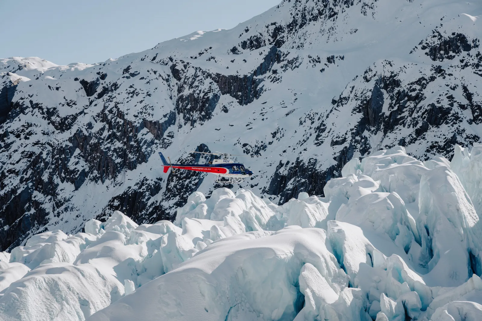 Helicopter with red markings flying over a dark ridge and a field of ice blocks