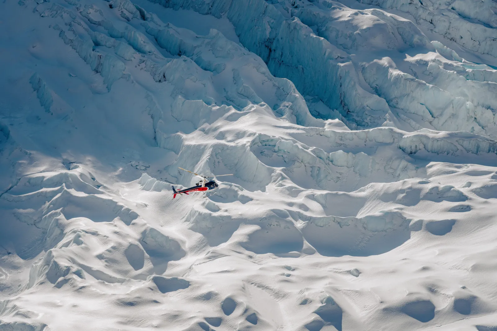 Small red helicopter on a crevassed snow surface seen from directly above