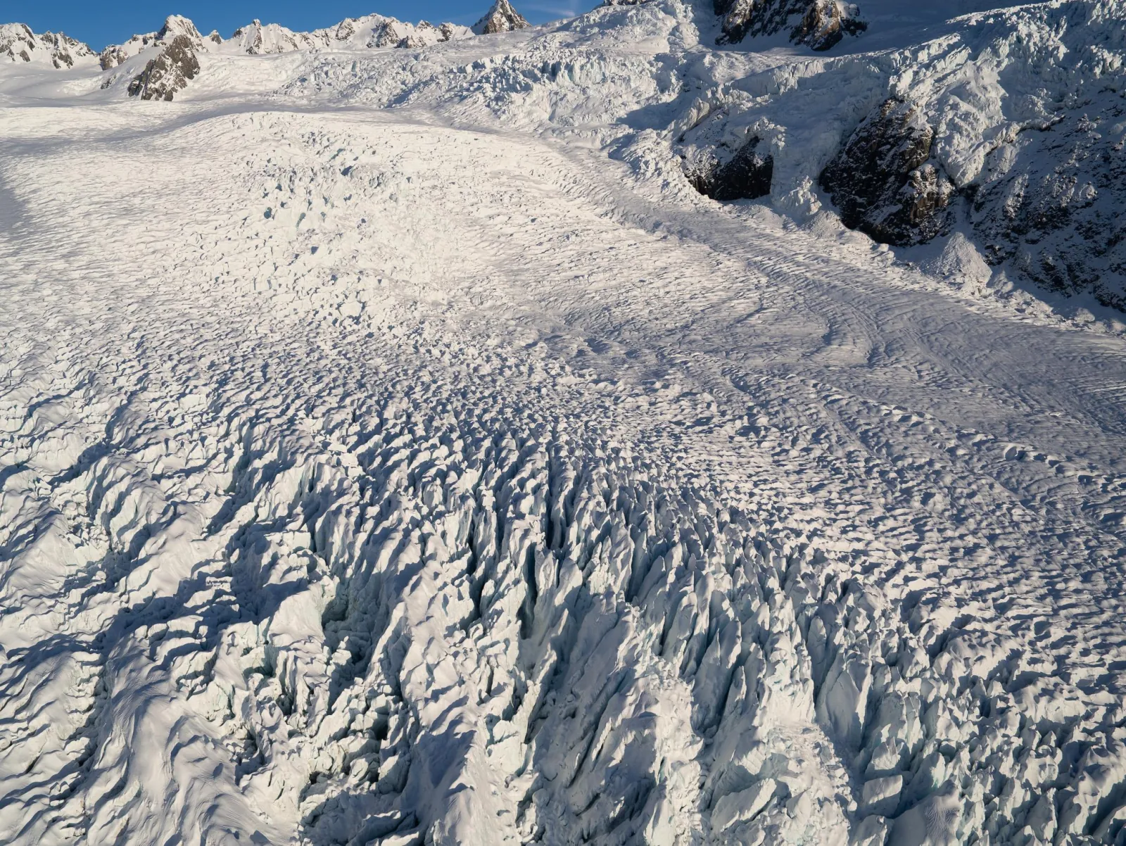 Aerial view of a wide glacier surface cut with fine crevasses and dark moraine