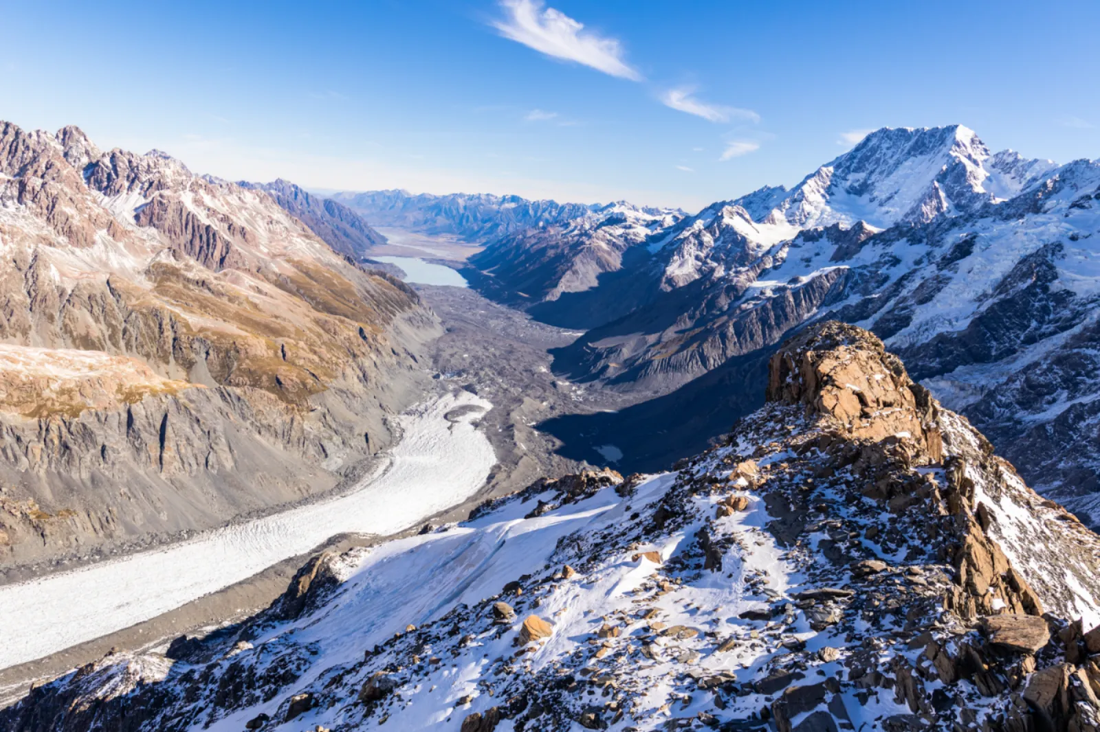 Aerial view of a long grey glacier valley running toward a lake and a high peak