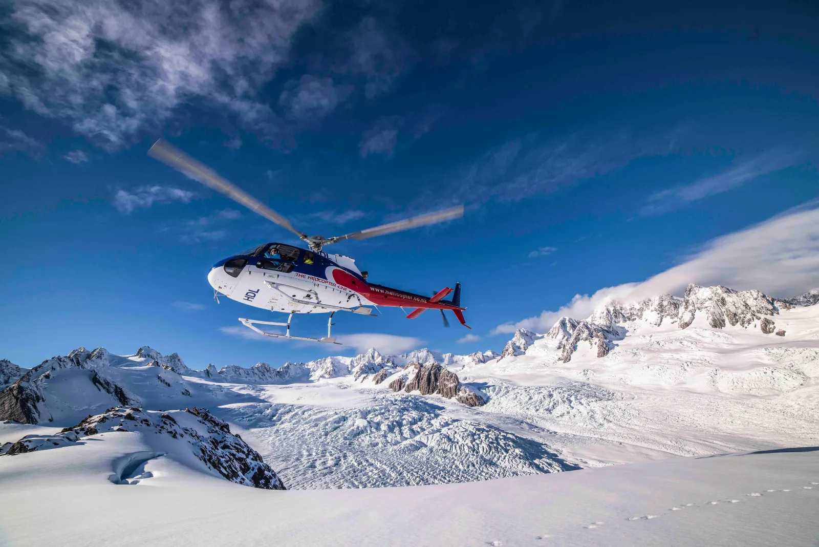 White and red helicopter in flight against deep blue sky above an alpine snowfield