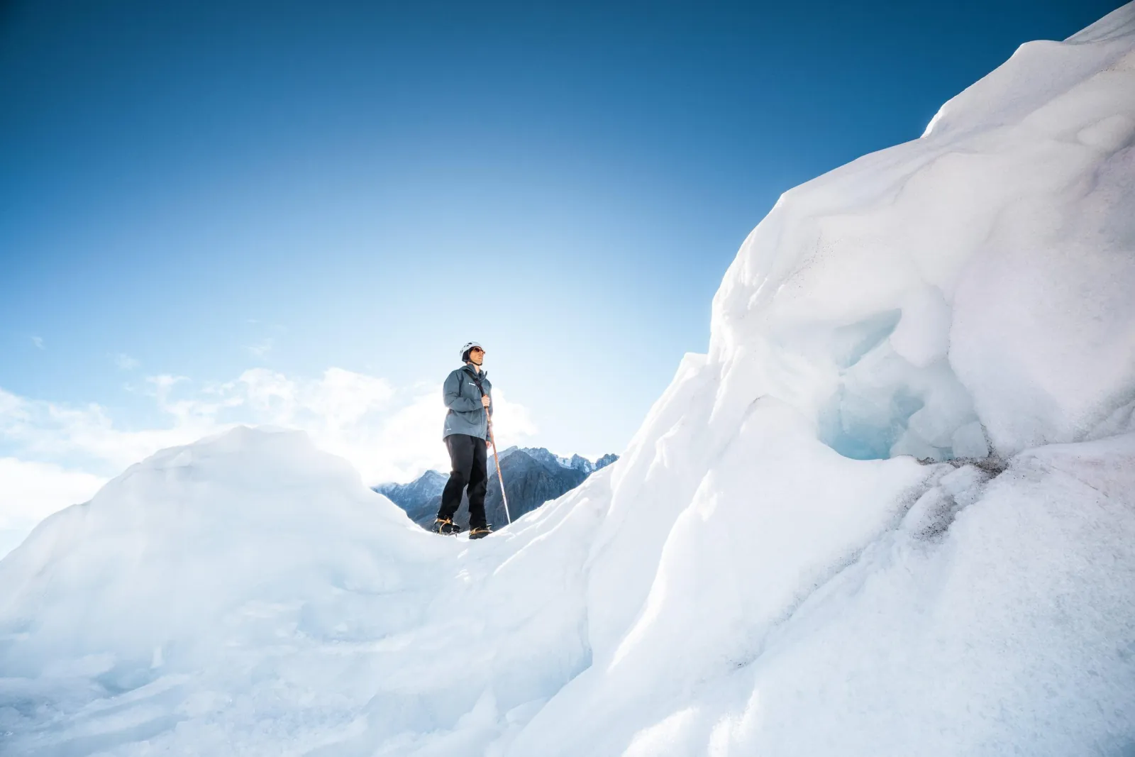 Lone hiker standing on top of a smooth ice ridge against deep blue sky