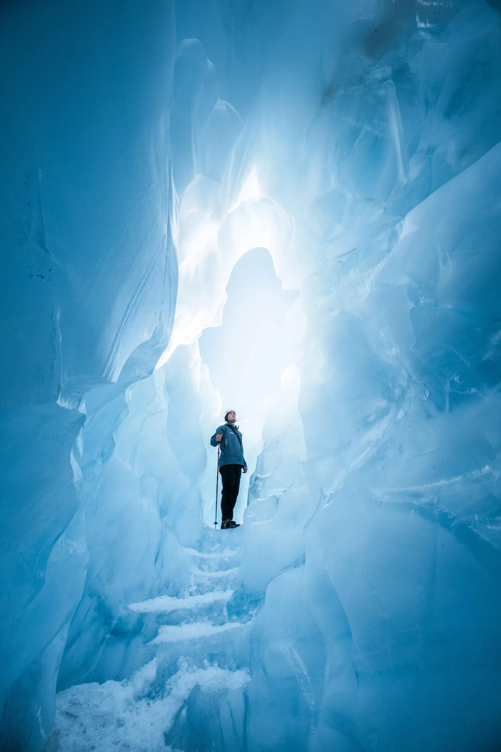 Small figure standing at the bottom of a tall luminous blue ice chasm