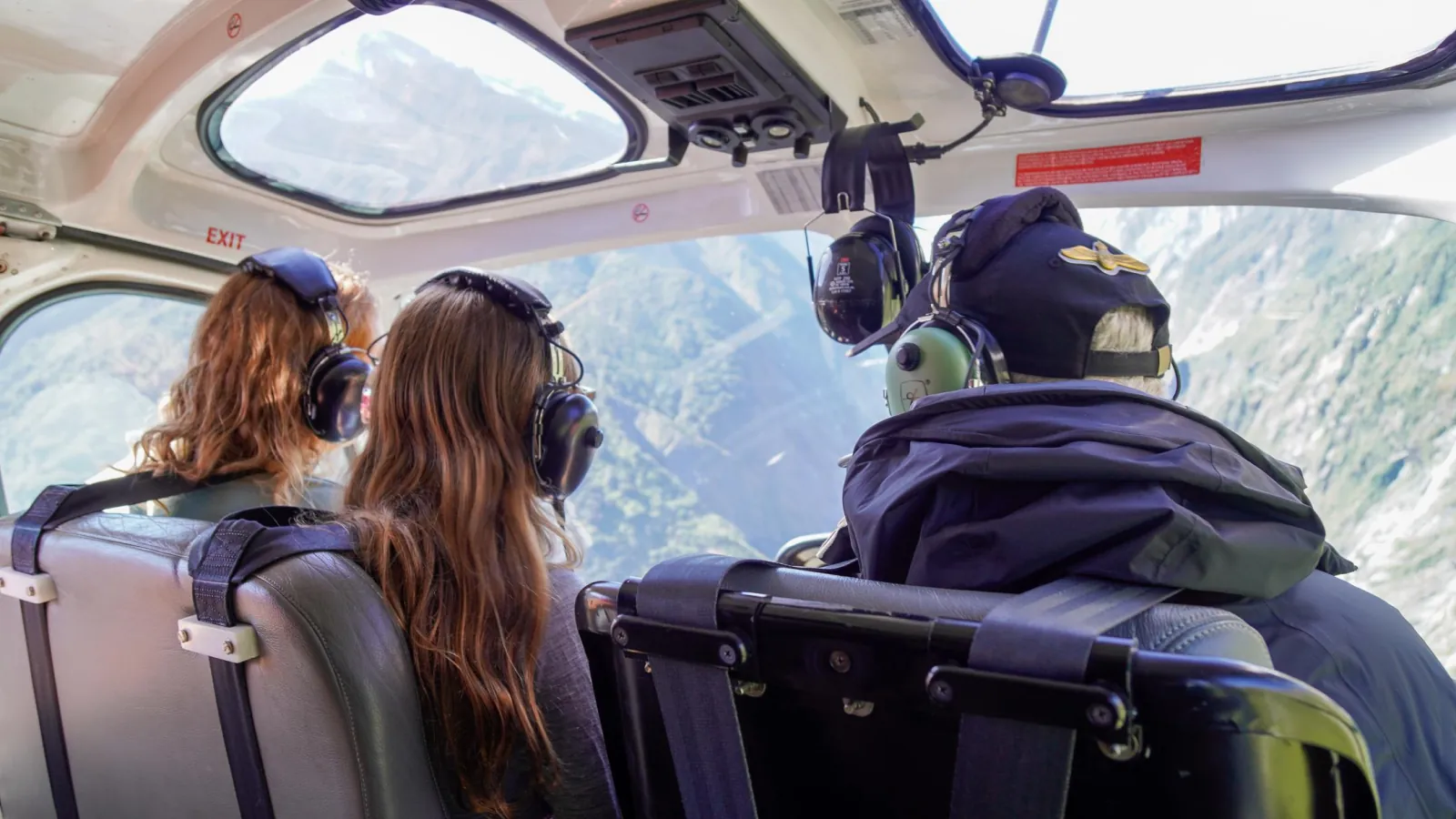 Rear view of two passengers and a pilot in headsets inside a helicopter cabin
