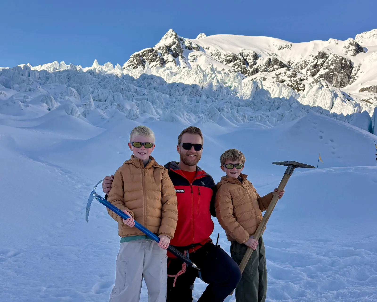 Guide in red jacket posing with two boys holding ice axes on snow